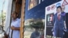 Libya -- A Libyan rebel stands by a shop window decorated with a portrait of Moammar Gadhafi with his son Seif al-Islam on his shoulders, in Tripoli, 25Aug2011